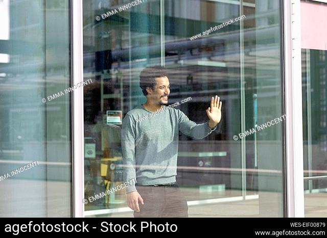 Smiling man looking away while touching glass wall