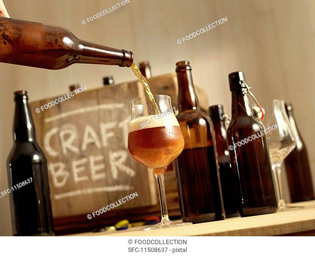 Beer being poured with open bottles of beer and a wooden crate labelled 'Craft Beer' in the background