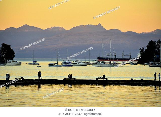 Nanaimo harbor, Vancouver Island , B.C., with people fishing on the fishing warf and boats moored in the calm water, against a mountain background