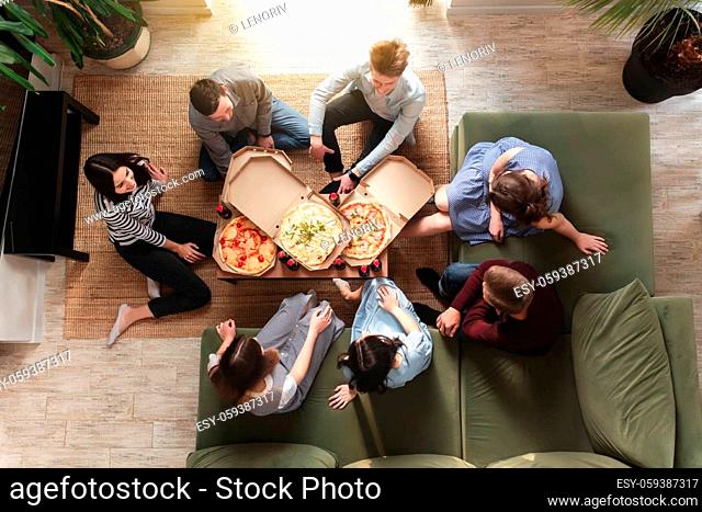 A pizza party, a group of friends chatting and happily eating pizza at the table and drinking sweet soda water. Top view from the second floor