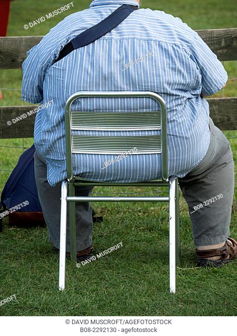 obese man sat on a small chair at an outdoor event, Britain