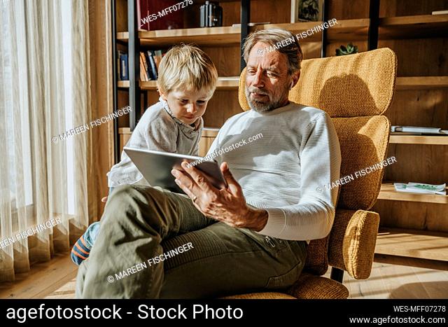 Curious boy looking while father using digital tablet at home