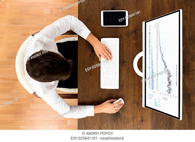 High Angle View Of Businessman Analyzing Graph On Desktop Computer