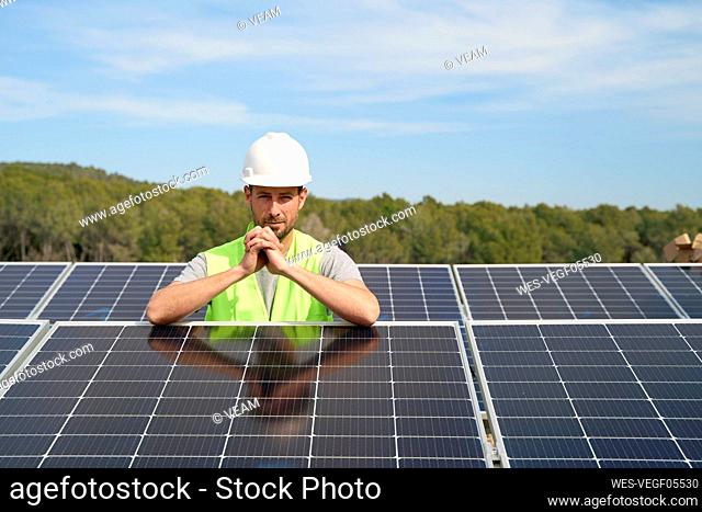 Engineer wearing hardhat standing with hands clasped between solar panels on roof