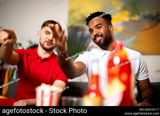 Smiling roommates talking with each other watching football match at home