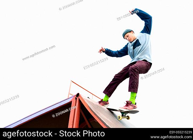 Teen skater in a hoodie sweatshirt and jeans slides over a ramp on a skateboard isolated on white