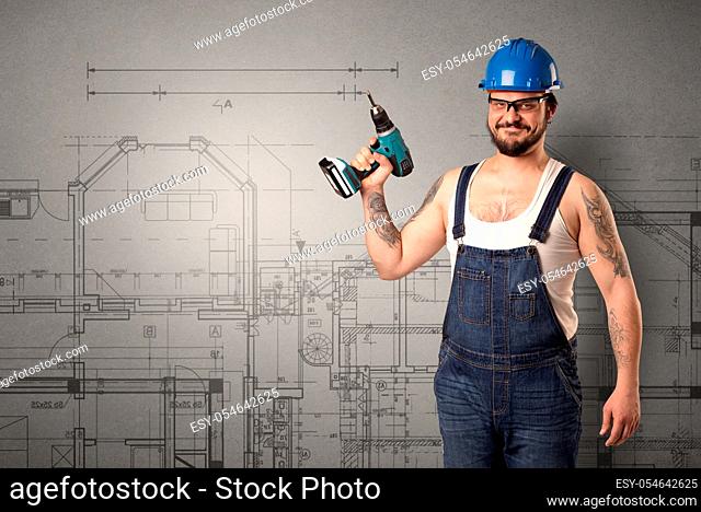 Worker standing with tool in his hand in front of technical drawings