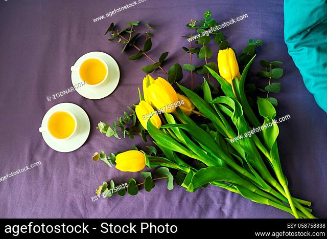 Yellow tulips and two cups of tea in bed, morning