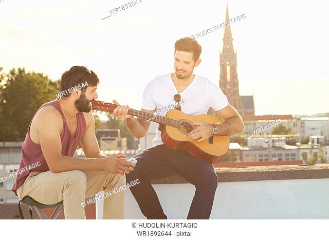 Young man with friend playing guitar at rooftop party