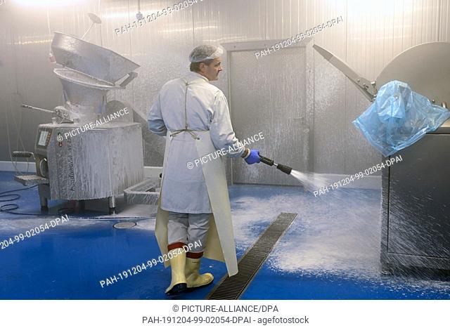 03 December 2019, Hessen, Usseln: An employee of ""Upländer Feinkost Waldecker Fleischwaren Heinrich Saure GmbH"" cleans the room with machines for sausage and...
