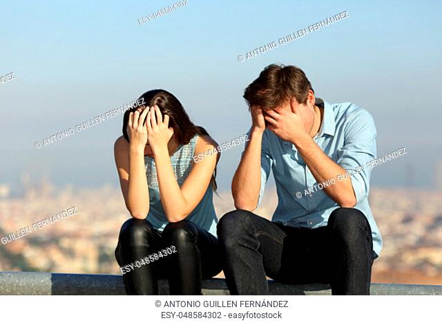 Sad couple complaining after argument sitting outdoors in a city ourskirts