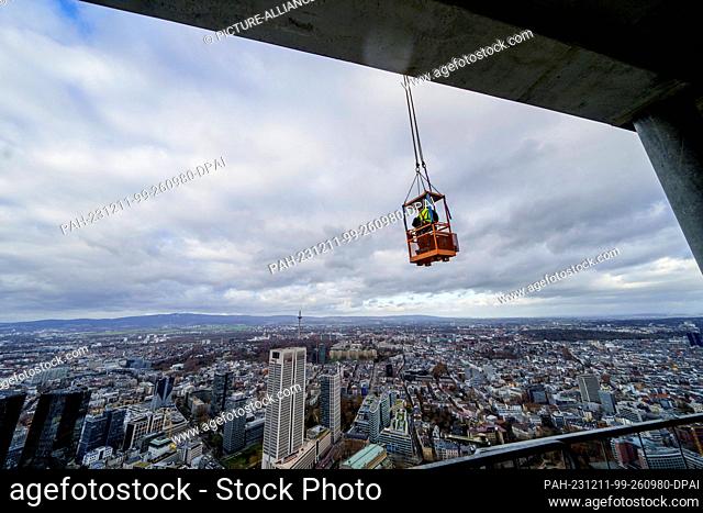 PRODUCTION - 11 December 2023, Hesse, Frankfurt/Main: On the 52nd floor, two men in a gondola are busy working on the exterior façade