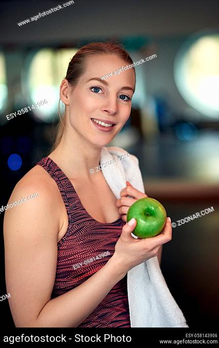 Attractive natural young woman athlete holding a fresh crisp green apple in her hand as she looks at the camera with a quiet smile in a healthy diet concept