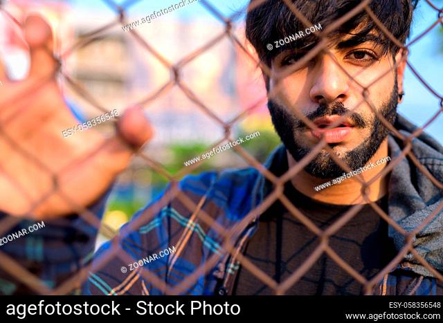 Portrait of young handsome bearded Indian hipster man in the city streets outdoors