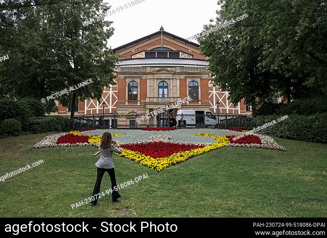 24 July 2023, Bavaria, Bayreuth: A woman takes a photo of the flowers and the Bayreuth Festival Hall. The 2023 Festival Open Air takes place at the foot of the...
