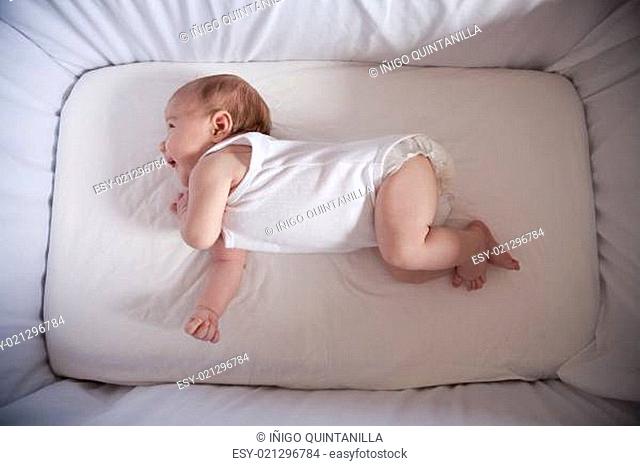 one month age newborn baby laughing lying in white cradle sheet