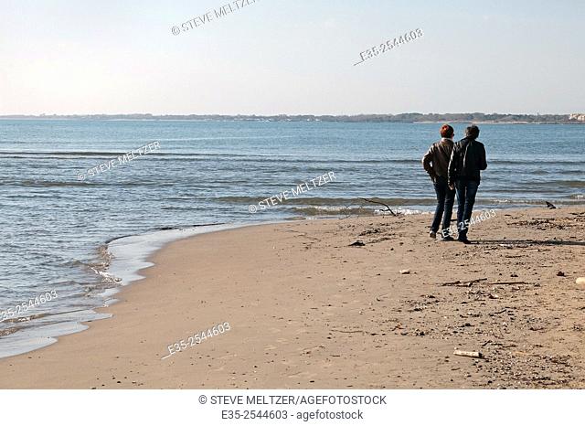 Two friends walk along a Mediterranean beach in autumn