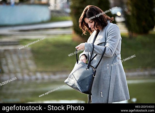 Woman with jacket checking purse by canal