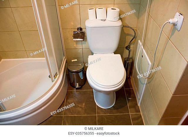 White toilet in it are three rolls of toilet paper near a shower is situated