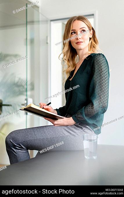 Businesswoman day dreaming while sitting with diary in office