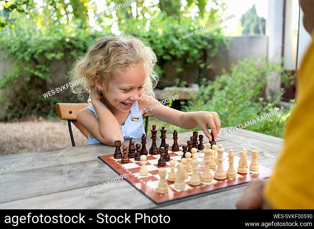 Happy blond girl playing chess in garden