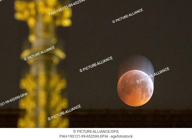 21 January 2019, Bavaria, Nürnberg: As a red, so-called ""blood moon"", the full moon stands behind the tip of the Beautiful Fountain