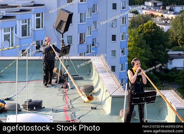 17 July 2021, Hamburg: Musicians blow their alphorns on the roof of a high-rise building while hundreds of spectators listen on a football pitch and all around