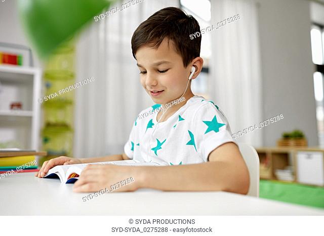 student boy in earphones reading book at home
