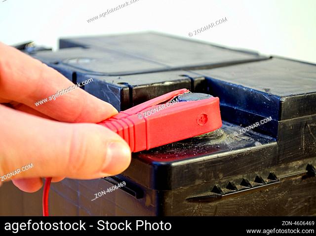closeup of hand plug car automobile battery charger red clamp on accumulator plus