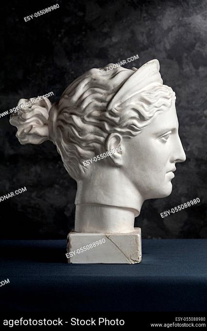White gypsum copy of ancient statue of Diana head for artists on a dark textured background. Plaster sculpture of woman face