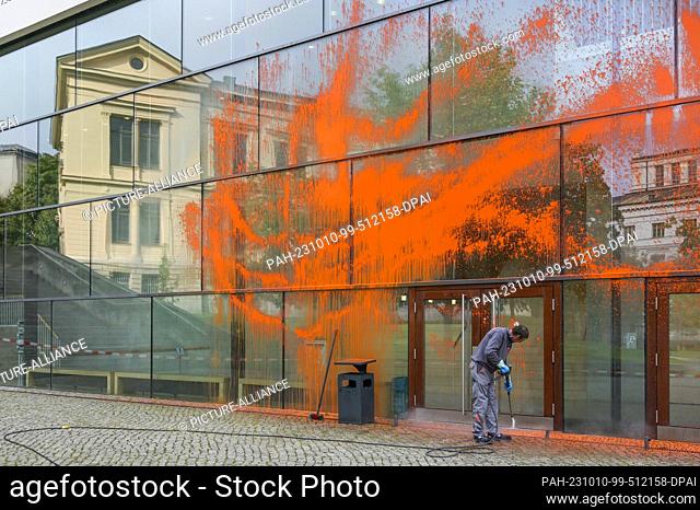 10 October 2023, Saxony-Anhalt, Halle (Saale): Using a high-pressure cleaner, an employee of a special company removes the orange paint from the glass facade
