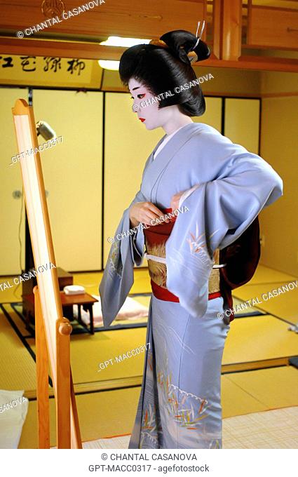 A GEIKO GEISHA DRESSING IN HER HOUSE OKIYA. THE GEIKO FIXES HER WIDE BELT OBI IN PLACE OVER HER KIMONO OBEBE, GION DISTRICT, KYOTO, JAPAN, ASIA