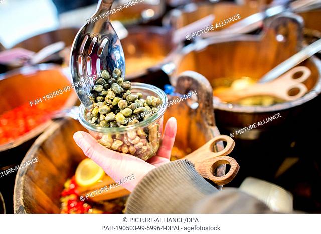 08 March 2019, Lower Saxony, Oldenburg: A woman fills fresh capers into a reusable glass at a weekly market in Bloherfelde