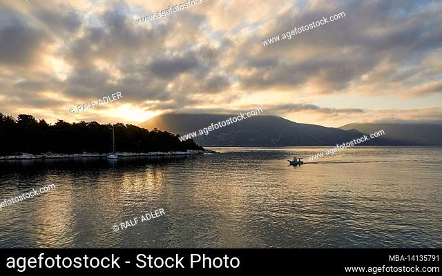 greece, greek islands, ionian islands, kefalonia, fiskardo, morning mood, partly cloudy sky, view of the sunrise over the harbor basin, gray cloud cover