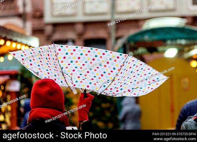 21 December 2023, Hesse, Frankfurt/Main: A woman walks through the Christmas market in the banking city with an umbrella