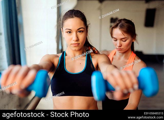 Young woman personal trainer helping with workout at gym. Woman doing exercises