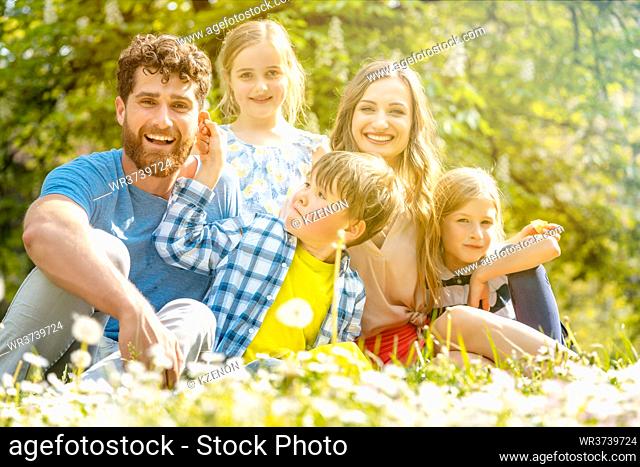 Family of five sitting on a meadow blowing dandelion flowers being happy and playful