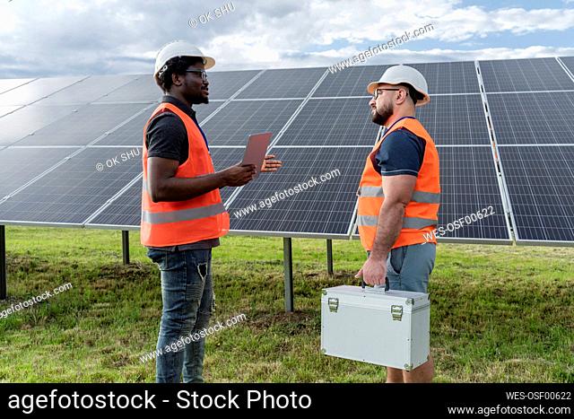 Engineer holding tablet PC discussing with coworker at solar station