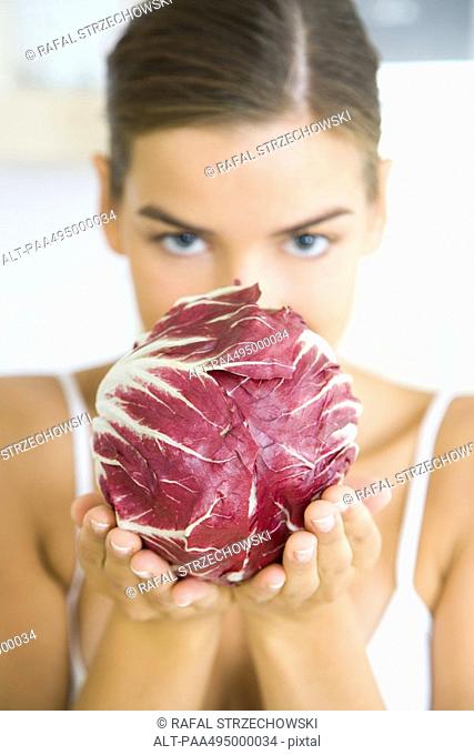 Woman holding a head of radicchio lettuce, partially obscuring her face, looking at camera