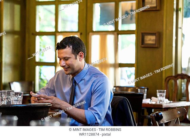 Business people outdoors, keeping in touch while on the go. A Latino man sitting at a table alone, checking his messages