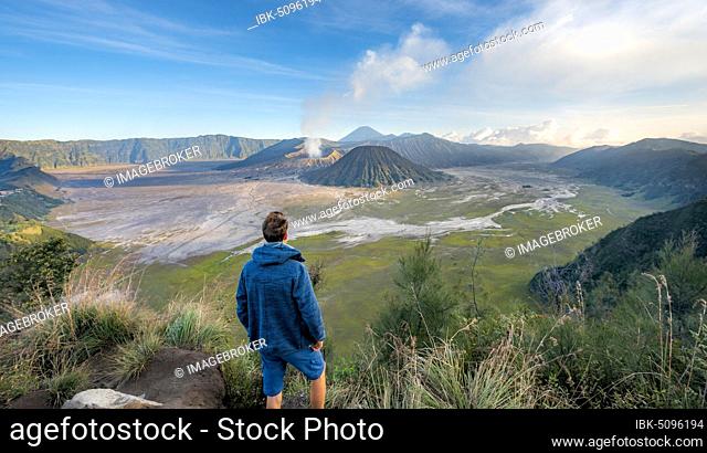 Young man in front of volcanic landscape, view in Tengger Caldera, smoking volcano Gunung Bromo, in front Mt. Batok, behind Mt. Kursi, Mt