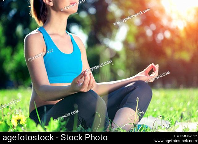 Girl meditates in lotus pose on green grass. Practicing of yoga concept. Young woman body in sportswear without head. Training and meditation outdoor at summer...