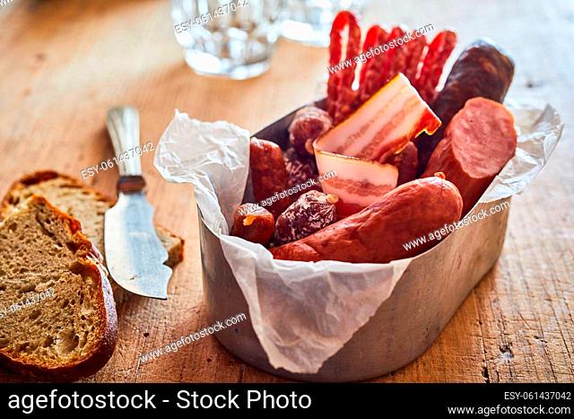 Various types of sausages and smoked lard served in metal container on wooden table with bread and sharp knife