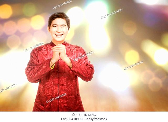 An Asian Chinese man in a cheongsam dress with congratulations gesture. Happy Chinese New Year
