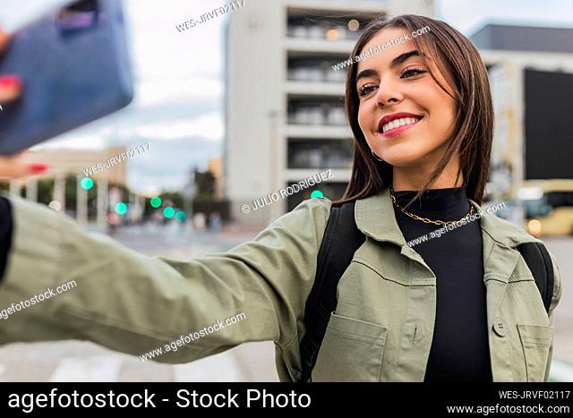 Smiling woman taking selfie through smart phone on road