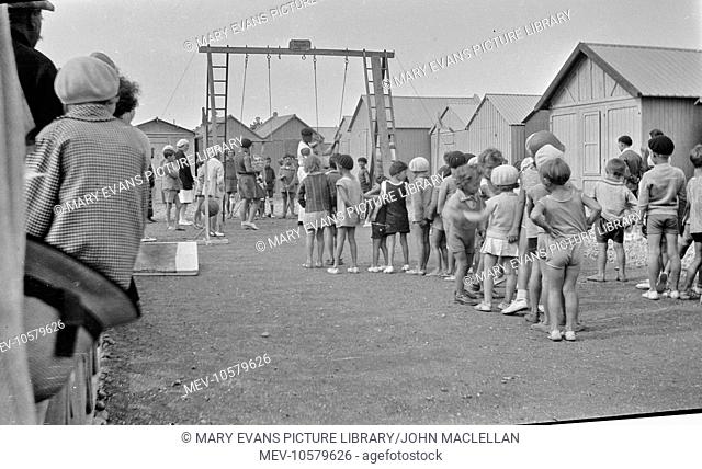 Children queueing up for a ride on the swings, probably at a seaside resort in France