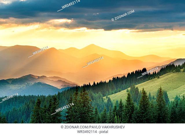 Mountains range with hills, sun, clouds and sky at sunset