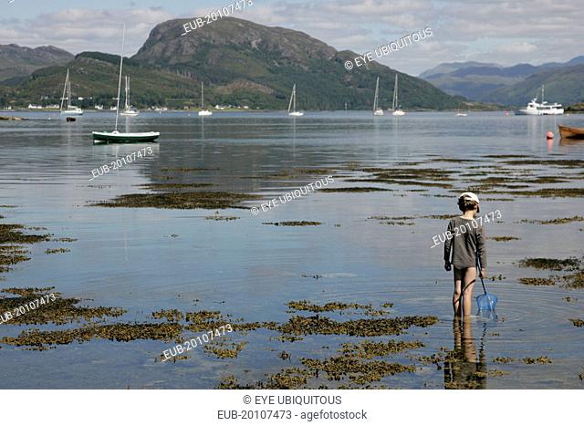 Young boy wading with fishing net in Loch Carron