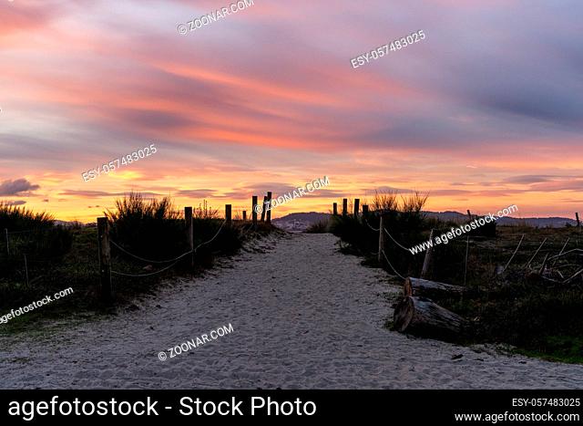 A sandy path and beach access leading through dunes under a colorful sunrise morning sky