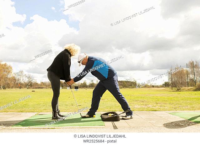 Man teaching friend to play golf at driving range